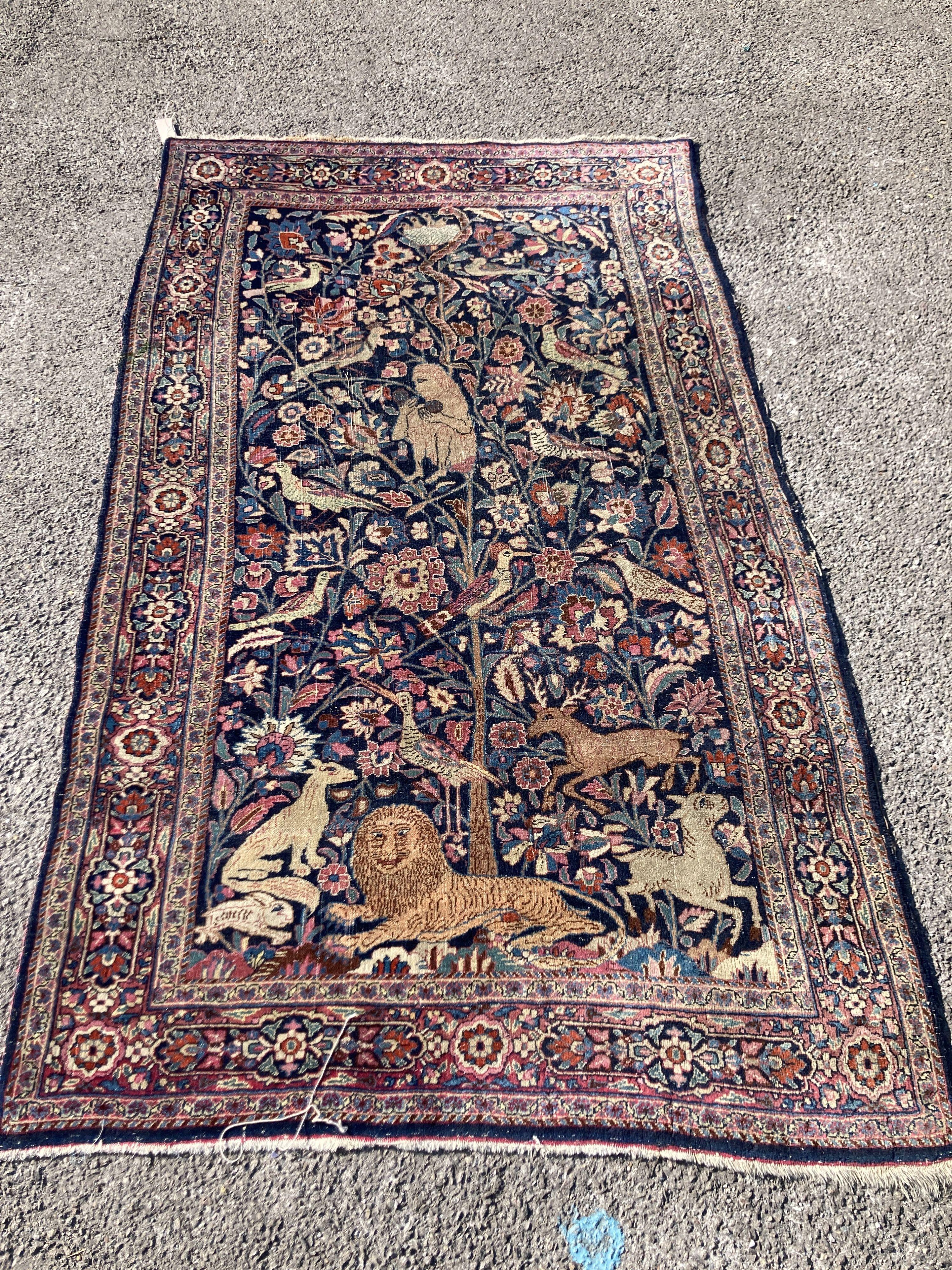 A Persian rug with a central Tree of Life interspersed with animals to include a seated monkey within the tree, a recumbent lion at the base, set within floral borders, 201 x 120cm